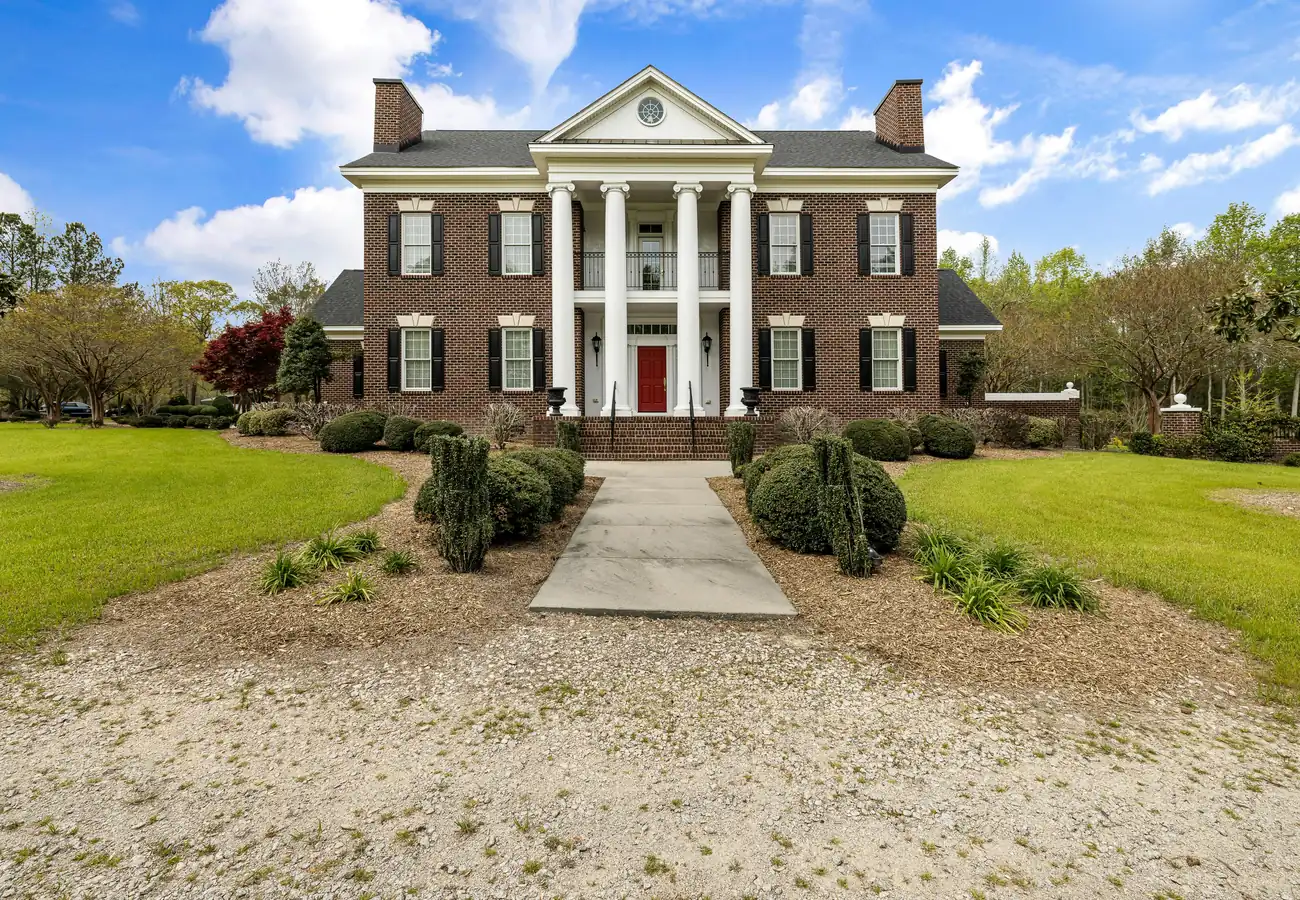 A columned brick colonial at the end of a gravel drive