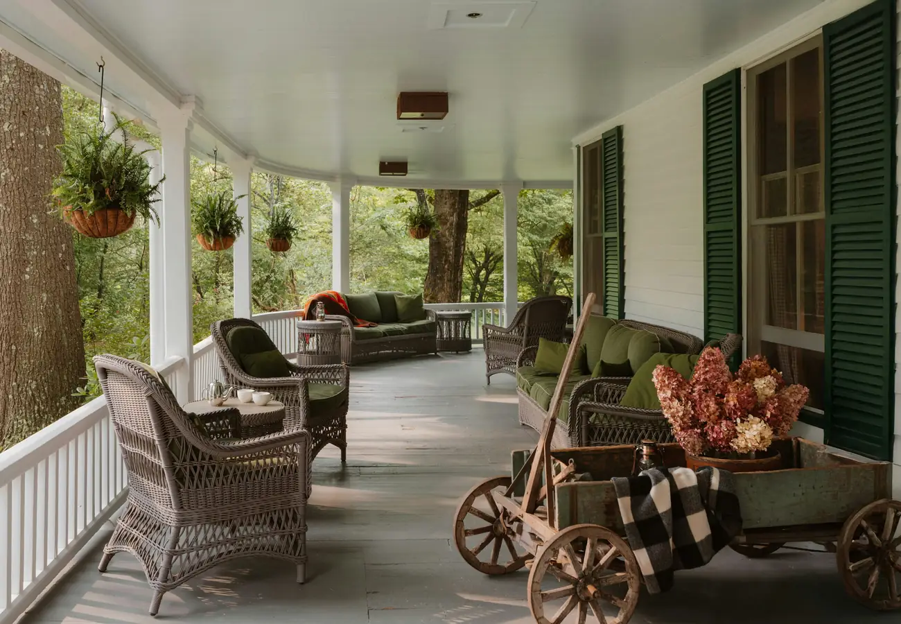 A wraparound porch with wicker seating and hanging baskets