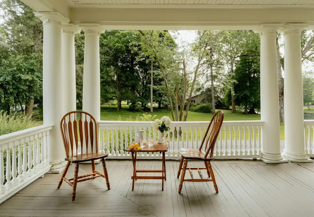 A columned porch with Windsor chairs looking out onto a lawn