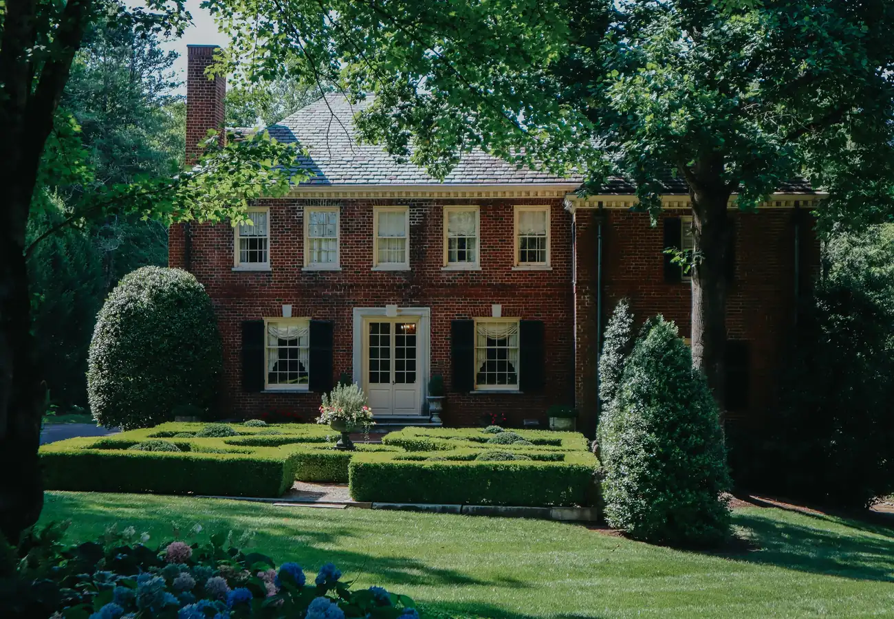 A brick colonial house behind a clipped boxwood garden