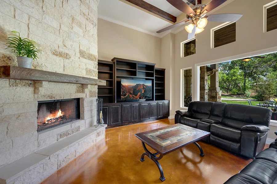 Living room with a limestone fireplace, wood beams, stained concrete floors and a view of the covered patio, representing buying a home in Whitney.