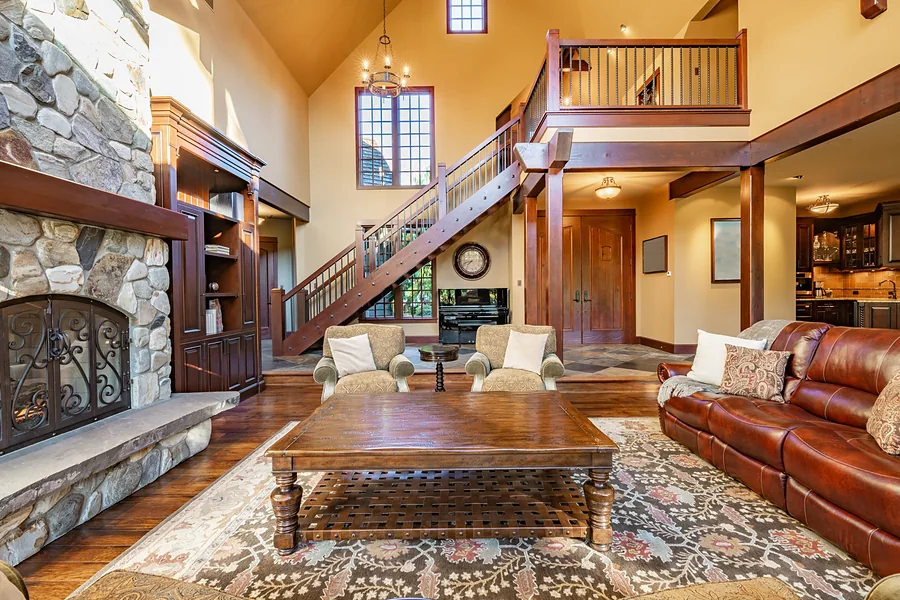 Great room with a river-rock fireplace, vaulted ceiling, open wood staircase and leather sofa, representing buying a home in Whitney.