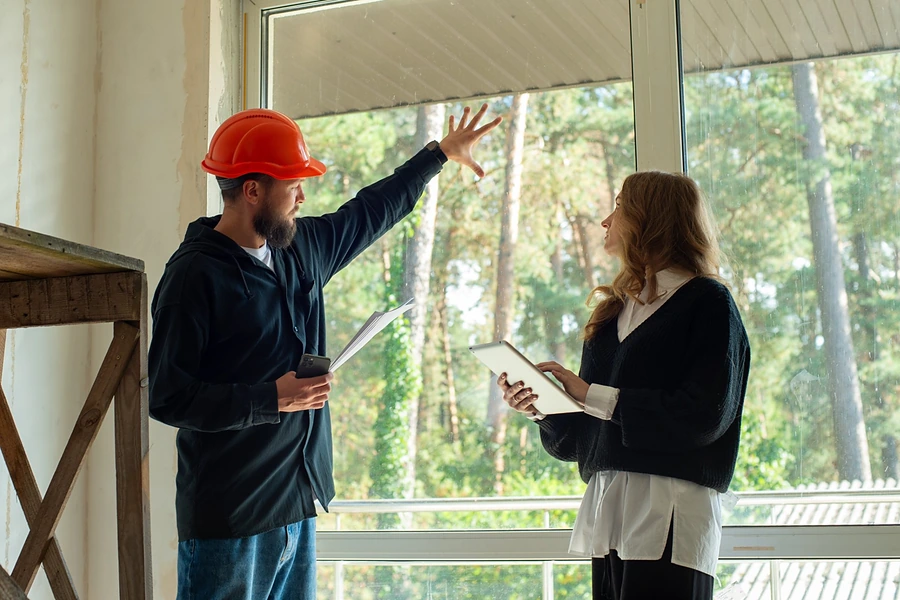 A contractor in a hard hat pointing out a large window during a walkthrough, representing a home inspection when buying a home in Whitney.