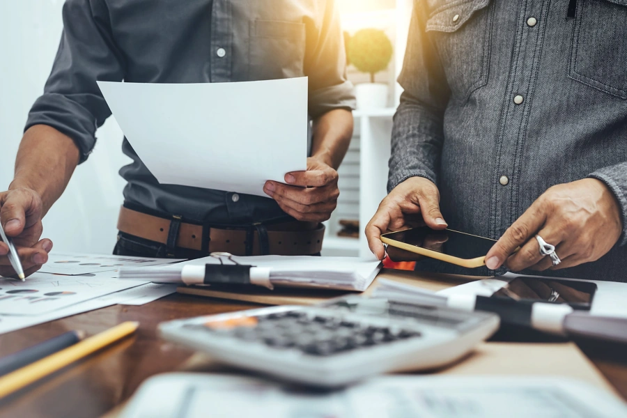 Two people reviewing paperwork, a phone and a calculator at a desk, representing getting pre-approved when buying a home in Whitney