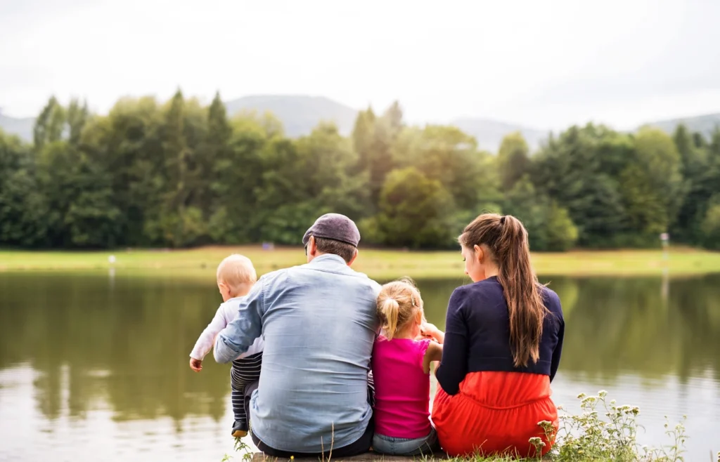 People sitting together on a lakeshore looking out over calm water and a tree line, representing lake homes for sale in Central Texas