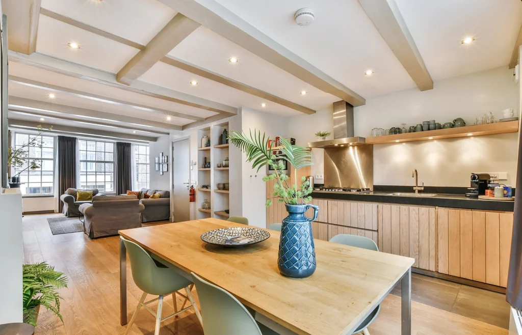 An open-plan kitchen and dining area with exposed ceiling beams, oak cabinetry and a living room beyond.