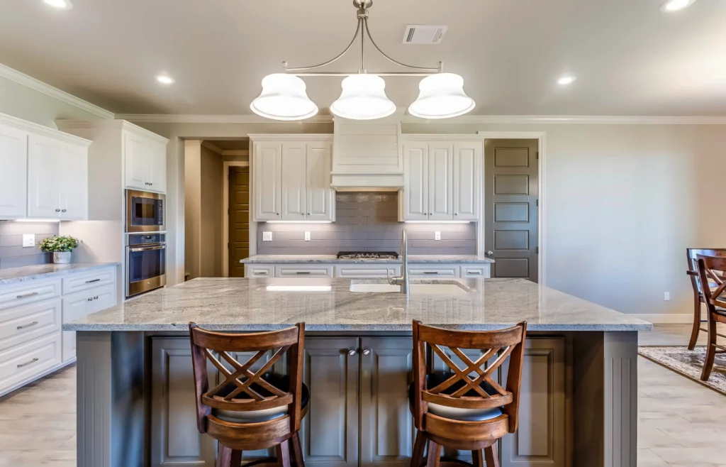 Bright kitchen with white cabinets, a granite island and wood bar stools, representing homes for sale in Central Texas