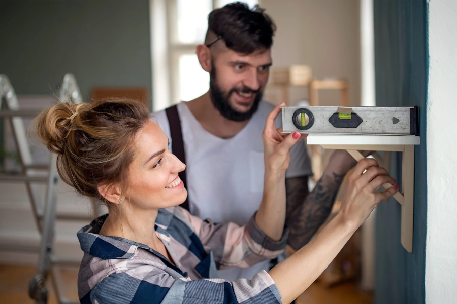 Couple using a level to hang a wall shelf, representing small repairs before selling a home in Whitney