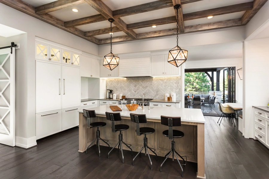 White kitchen with wood ceiling beams, a large island and pendant lights, representing listing photography when selling a home in Whitney