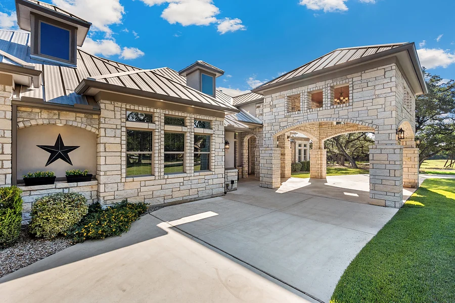Limestone home with a standing-seam metal roof and an arched stone porte-cochere under live oaks, representing selling a home in Whitney.