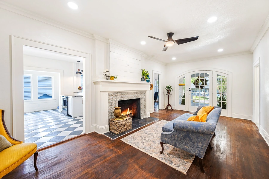 Bright living room with a tiled fireplace, original hardwood floors and arched French doors, representing selling a home in Whitney.