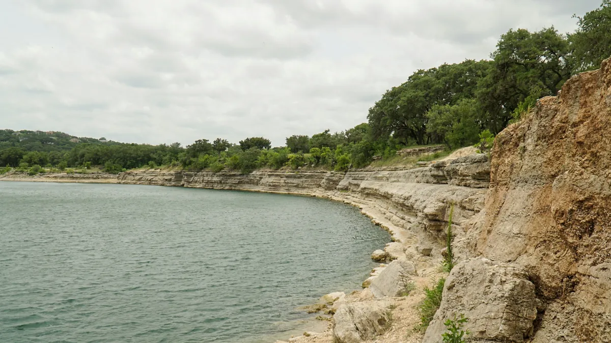 Limestone bluffs and live oaks curving along a lake shoreline under a cloudy sky, representing the water near White Bluff homes for sale